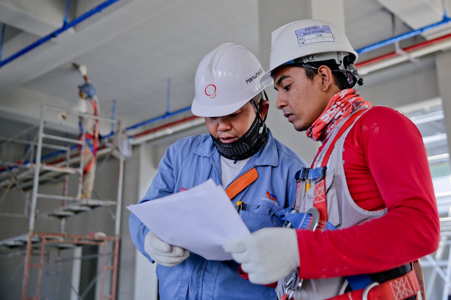 Two workers are reviewing a document while wearing safety gear